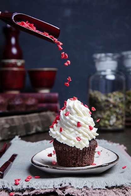 Concepto de comida voladora. Decoraciones navideñas para pastel vertido en crema fresca sobre cupcake. Postre de tarta casera fresca para año nuevo en decoración con libro y té. vertical. malhumorado oscuro