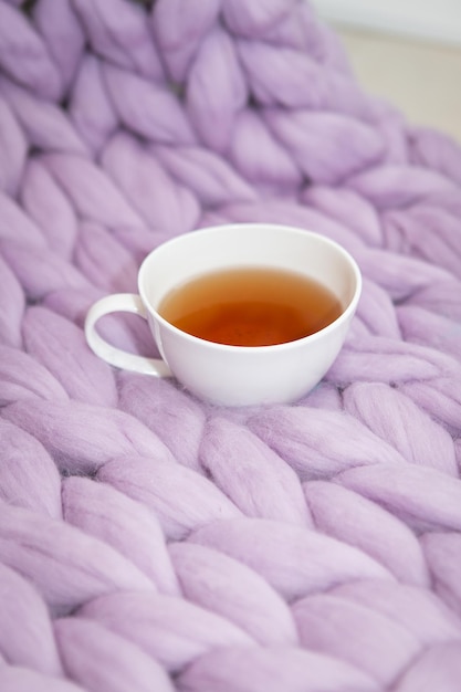 El concepto de comodidad y comodidad es una manta de punto de lavanda rosa con una taza blanca de té caliente en ella Lugar para la inscripción de la foto vertical