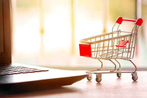 Concepto de compra online. Carro de compras, cajas pequeñas, laptop en el escritorio.