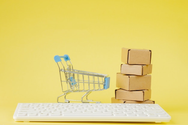 Concepto de compra online. Carro de compras con pequeñas cajas en el interior sobre fondo amarillo