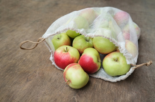 Concepto de compra de residuos cero. Manzanas orgánicas frescas en malla reutilizable producen bolsa en mesa de madera