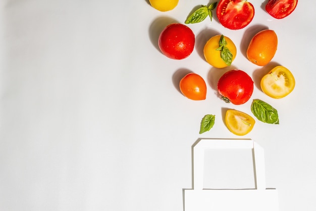 Concepto de compra de residuos cero. Tomates maduros surtidos con hojas de albahaca fresca. Luz dura de moda, sombra oscura, vista superior