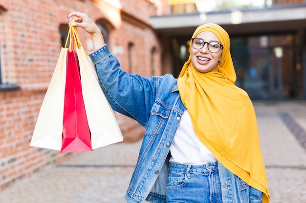 Concepto de compra y venta - Feliz niña musulmana árabe con bolsas de compras después del centro comercial