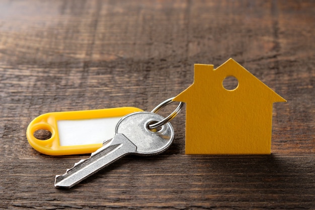 Foto concepto de compra de una vivienda. llaves con llavero y una casa sobre un fondo de madera marrón.