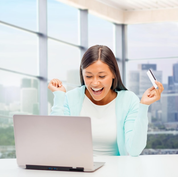 concepto de compras, banca, negocios y personas en línea: mujer de negocios feliz con computadora portátil y tarjeta de crédito sobre el fondo de la ventana de la oficina