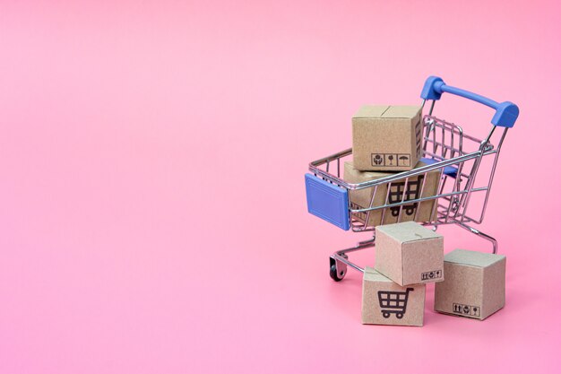 Concepto de compras: cartones o cajas de papel en el carrito azul sobre fondo rosa. los consumidores de compras en línea pueden comprar desde casa y servicio de entrega. con espacio de copia