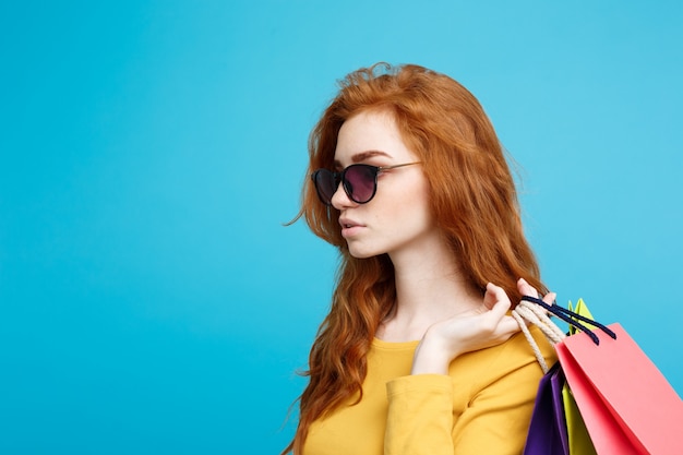 Concepto de Compras - Close up Retrato joven atractiva hermosa redhair niña sonriente mirando a la cámara con bolsa de la compra. Fondo En Pastel Azul. Copie el espacio.