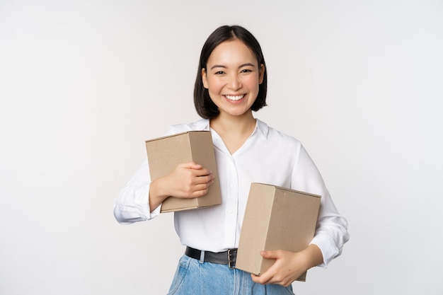 Concepto de compras y entrega Joven mujer asiática feliz posando con cajas y sonriendo de pie sobre fondo blanco.