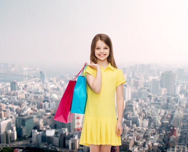 concepto de compras, felicidad y personas - niña sonriente con vestido amarillo con bolsas de compras