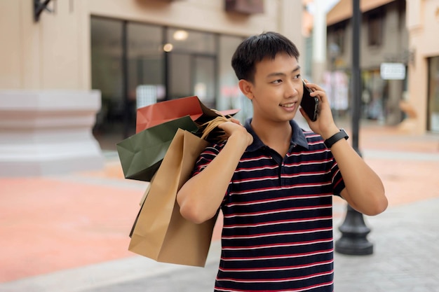 Concepto de compras El hombre de camisa azul marino y rojo con rayas horizontales que lleva sus bolsas de la compra en la espalda mientras realiza una llamada telefónica.