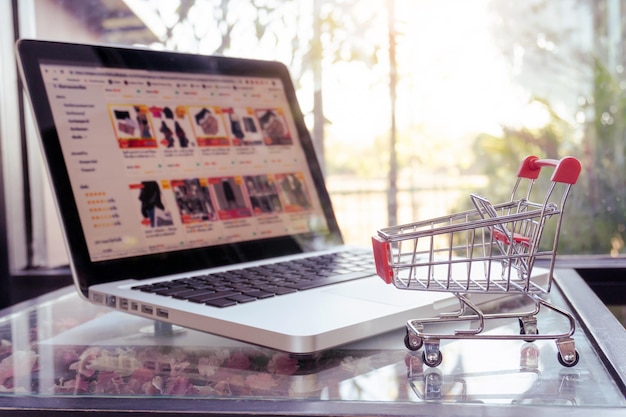 Concepto de compras en línea carrito de compras o carrito y computadora portátil en la mesa