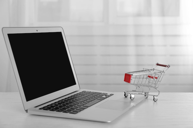 Concepto de compras en línea Laptop con mini carrito de mercado en una mesa de madera