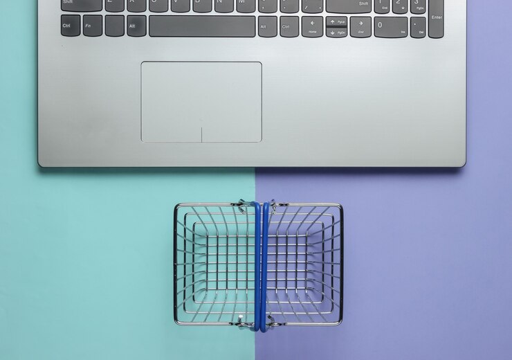 Foto concepto de compras en línea laptop y mini cesta de la compra sobre fondo pastel azul violeta