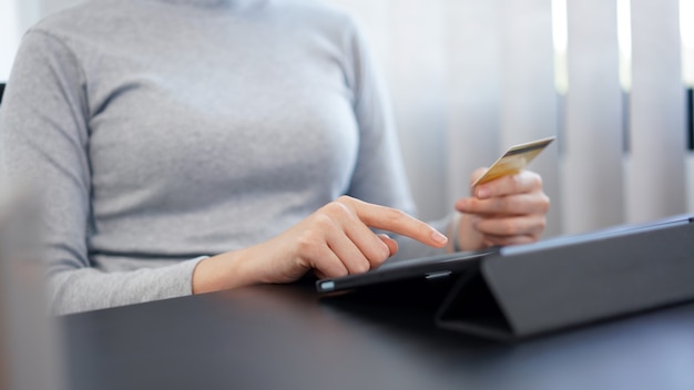 Concepto de compras en línea una mujer adulta media usando su tarjeta de crédito para hacer una transacción financiera en su ipad.