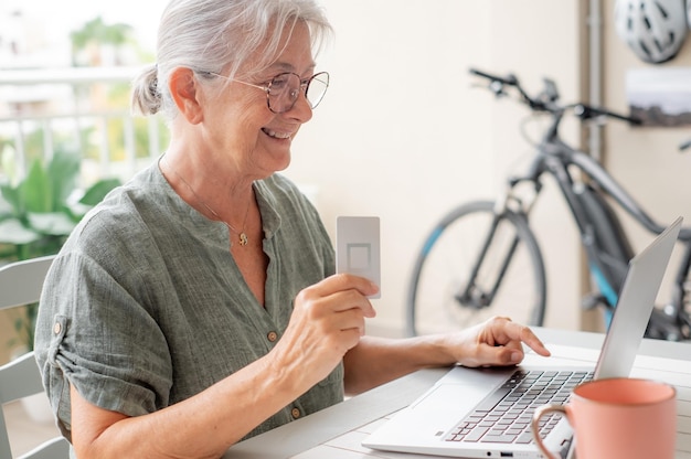 Concepto de compras en línea Mujer anciana feliz usando portátil con tarjeta de crédito lista para hacer compras