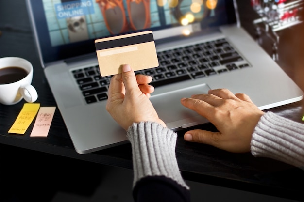 Concepto de compras en línea. Mujer con tarjeta de crédito oro en la mano y compras en línea