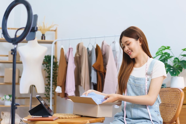 Concepto de compras en línea Mujeres asiáticas empacando vestidos en cajas de paquetes después de transmitir en vivo vendiendo ropa