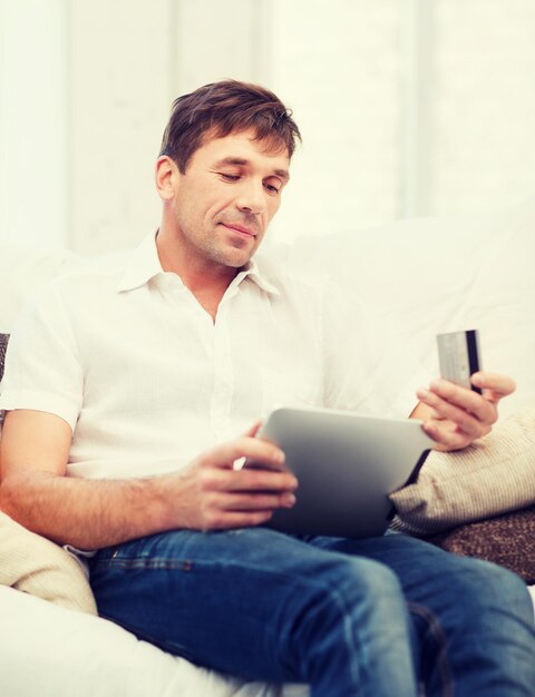 Concepto de compras en línea o por Internet - hombre sonriente con tablet pc y tarjeta de crédito en casa