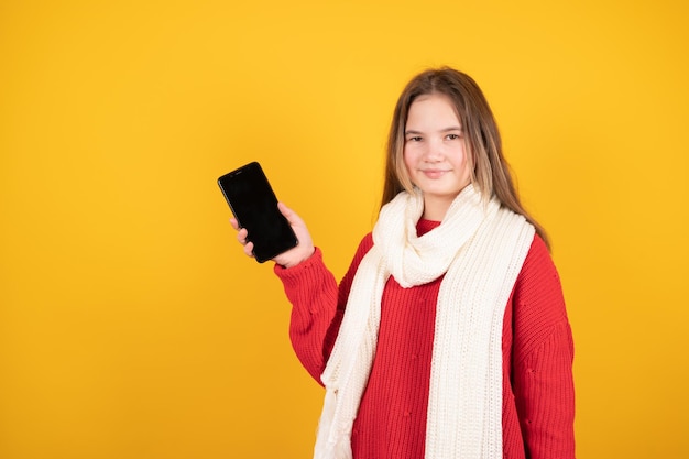 Concepto de compras en línea Smilling jovencita que muestra el fondo amarillo de la pantalla del teléfono inteligente vacía