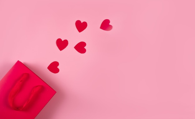 Concepto de compras en línea. Vista superior de la bolsa de regalo y corazones de papel rosa sobre fondo rosa, espacio de copia, capa plana. Fondo para el día de San Valentín, cumpleaños, día de la madre