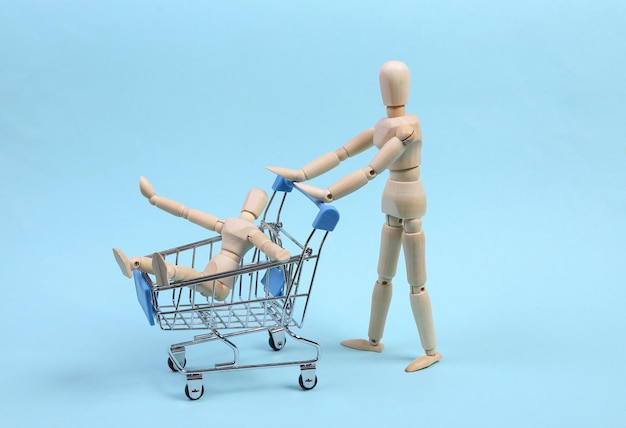 Concepto de compras. Marionetas de madera con carrito de supermercado sobre fondo azul. Pasando tiempo juntos