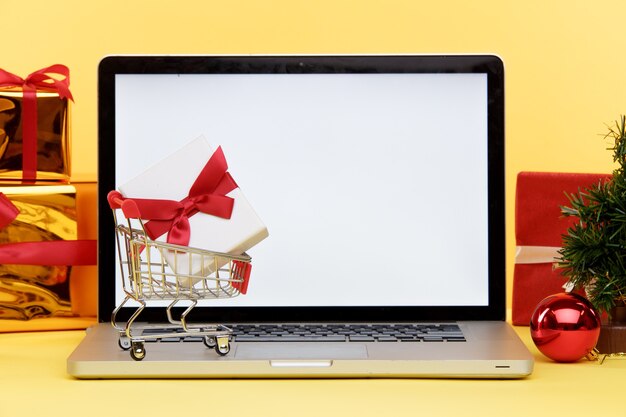 Concepto de compras navideñas en línea en la pantalla del portátil. Pantalla blanca en la computadora y regalos con bolsas de papel cerca.