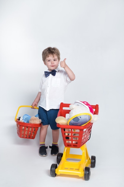 Concepto de compras niño con cesta de la compra y carro de compras dando pulgar hacia arriba niño con niño