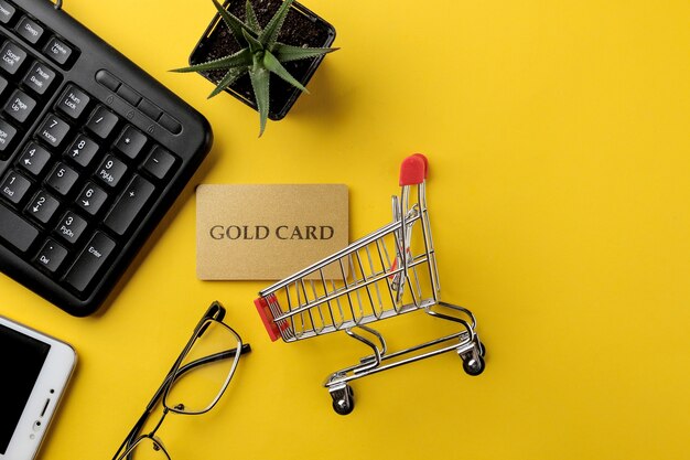 El concepto de compras online. Composición con una tarjeta de descuento y un carrito de la compra y un teléfono sobre un fondo amarillo