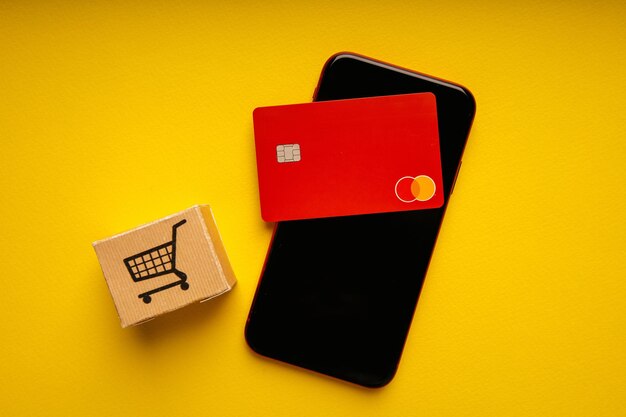 Concepto de compras y pagos en línea desde tarjetas de crédito Caja de entrega con carro y teléfono inteligente
