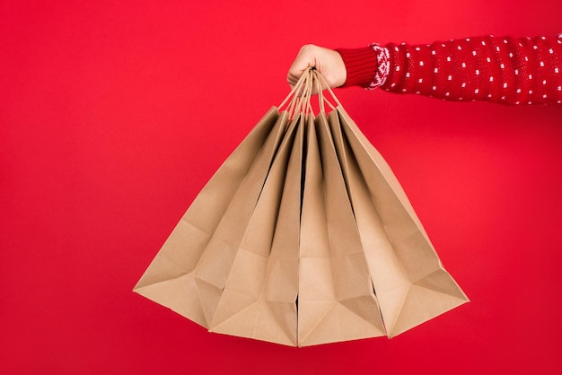 Foto concepto de compras de vacaciones de invierno. cerrar foto de hombres en suéter rojo sosteniendo cuatro bolsas de papel aisladas sobre fondo rojo.