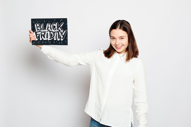 Concepto de compras, venta al por menor, viernes negro, venta, compras y personas - joven morena sonriente está sosteniendo un cartel de viernes negro. Venta de viernes negro.