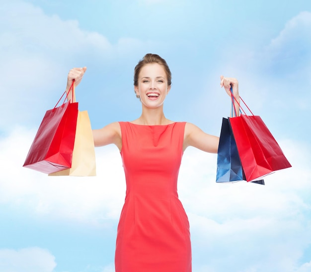 concepto de compras, venta, navidad y vacaciones - mujer elegante riendo vestida de rojo con bolsas de compras