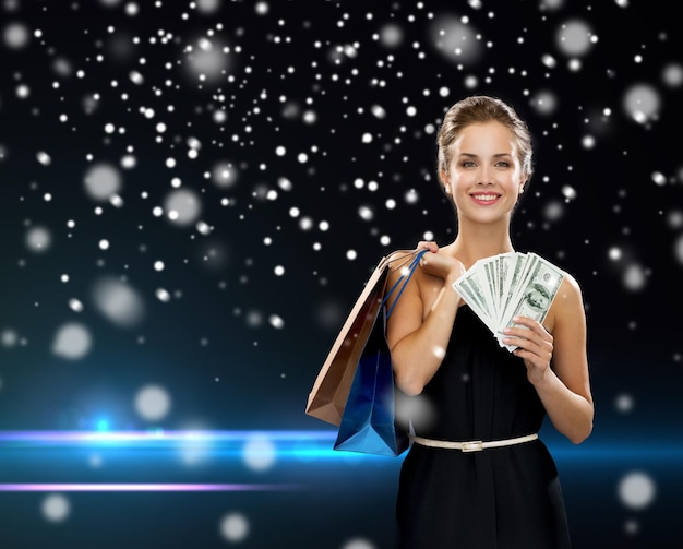 concepto de compras, venta, regalos, dinero y vacaciones - mujer sonriente vestida con bolsas de compras y dinero sobre fondo negro