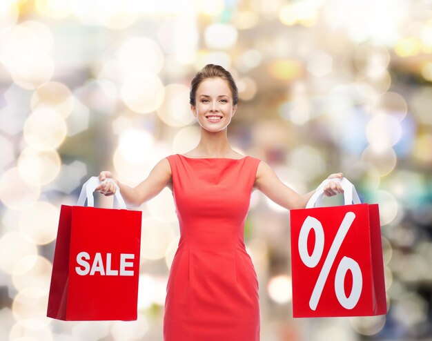 concepto de compras, venta, regalos, navidad y vacaciones - mujer joven sonriente vestida de rojo con bolsas de compras con signo de porcentaje y venta