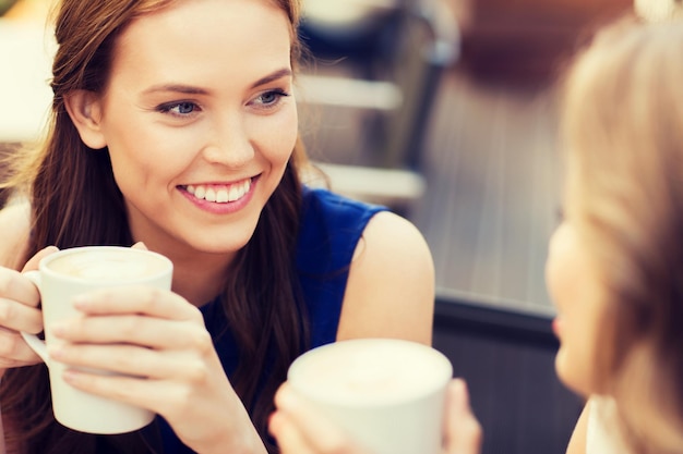 concepto de comunicación y amistad - mujeres jóvenes sonrientes con tazas de café en el café