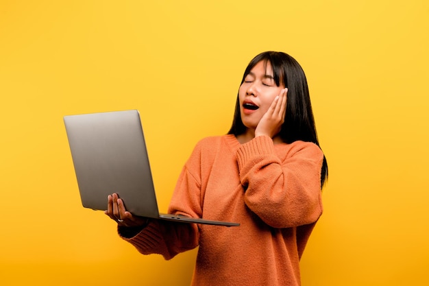 Concepto de comunicación en línea chica asiática usa laptop en casa foto de estudio amarilla Está feliz de pasar su tiempo libre en línea mientras chatea con amigos en las redes sociales comprando o trabajando en línea