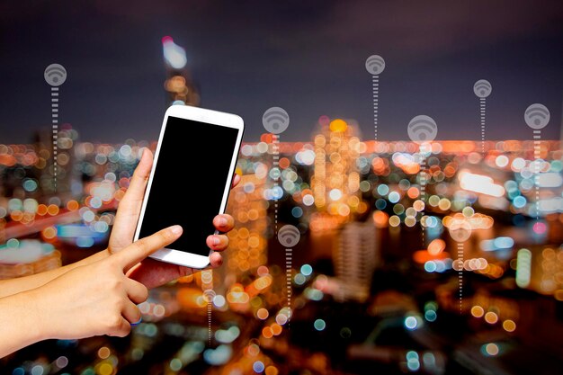 Foto concepto de conexión y tecnología sosteniendo el teléfono y presionando la pantalla en el fondo de la ciudad nocturna