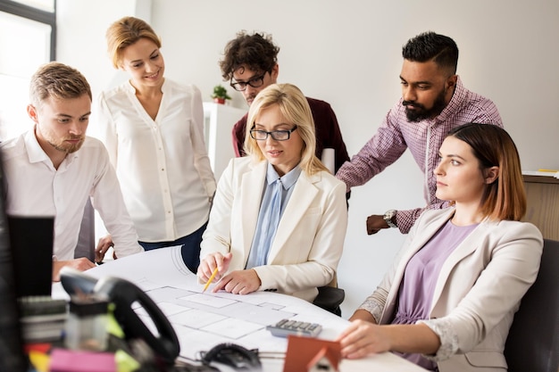 concepto de construcción, construcción, arquitectura, bienes raíces y personas: equipo de negocios con reunión de planos y discusión del proyecto de la casa en la oficina