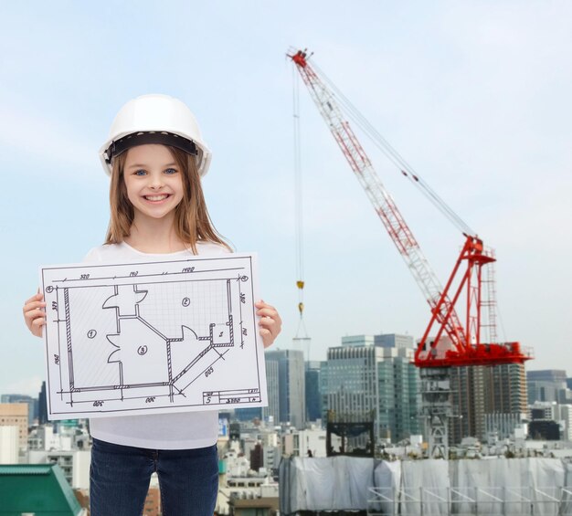 concepto de construcción, desarrollo, construcción y arquitectura - niñita sonriente con casco blanco que muestra planos