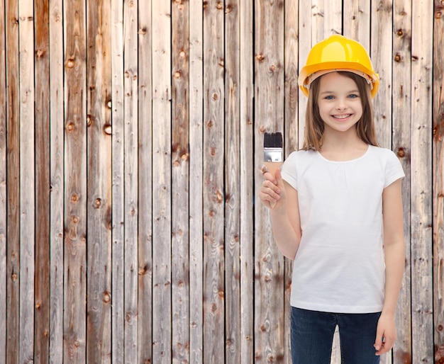 concepto de construcción y personas - niña sonriente en casco protector con pincel