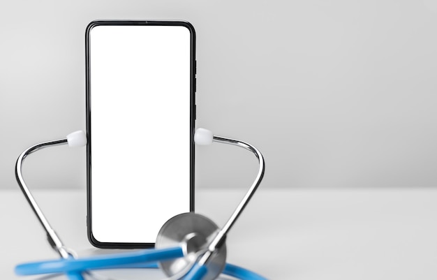 Foto concepto de consulta médica en línea. estetoscopio y teléfono celular sobre fondo gris. maqueta de teléfono de salud de la aplicación. copie el espacio