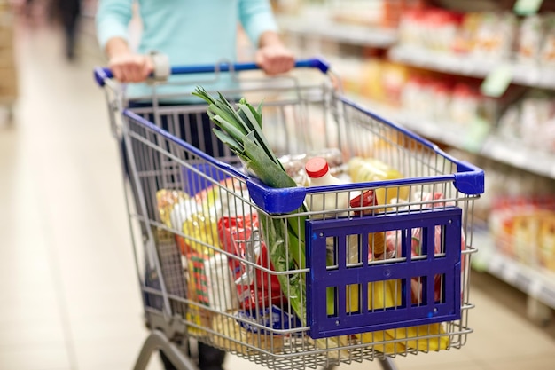Concepto de consumismo y personas: mujer con carrito de compras o carrito comprando comida en una tienda de comestibles o supermercado