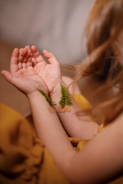 Concepto contra la vacunación, la depresión, el suicidio, el primer plano de las manos de una niña con ramitas de helecho pegadas con tiritas en las venas.