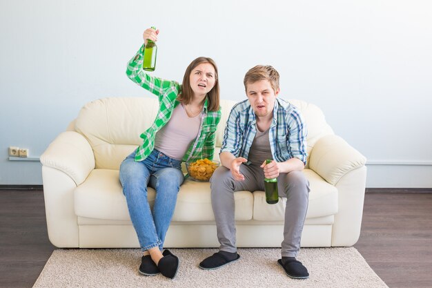 Concepto de copa mundial de fútbol - pareja de amigos sentados en el sofá viendo el juego deportivo en la televisión