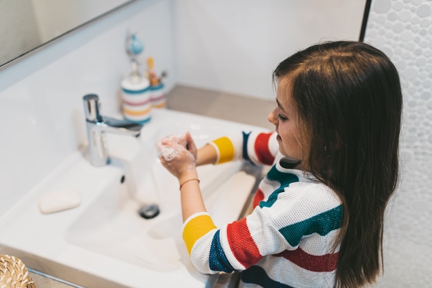 Concepto de coronavirus COVID-19. Chica lavándose las manos en el baño con jabón antibacteriano.