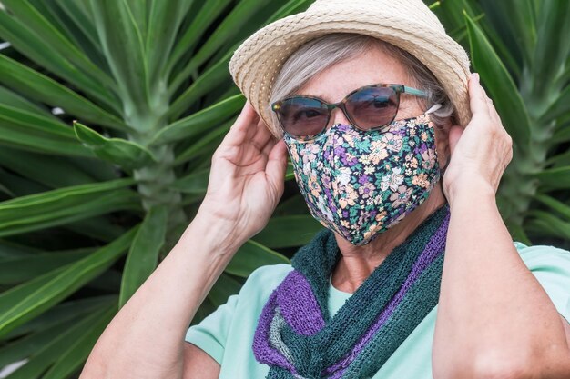 Concepto de coronavirus Retrato de mujer adulta mayor con sombrero de paja con máscara protectora floreada