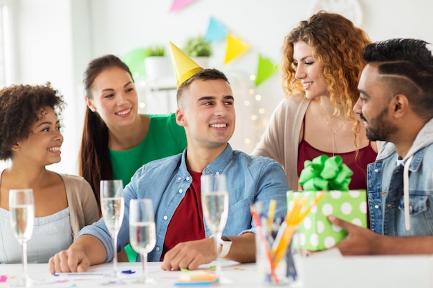 Foto concepto corporativo, de celebración y de personas - equipo feliz con regalos y copas de champán saludando a un colega en la fiesta de cumpleaños de la oficina