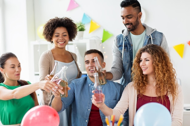 Foto concepto corporativo, de celebración y de vacaciones - equipo feliz haciendo sonar botellas con bebidas no alcohólicas en la fiesta de la oficina