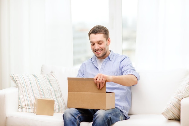 concepto de correos, hogar y estilo de vida - hombre sonriente con cajas de cartón en casa