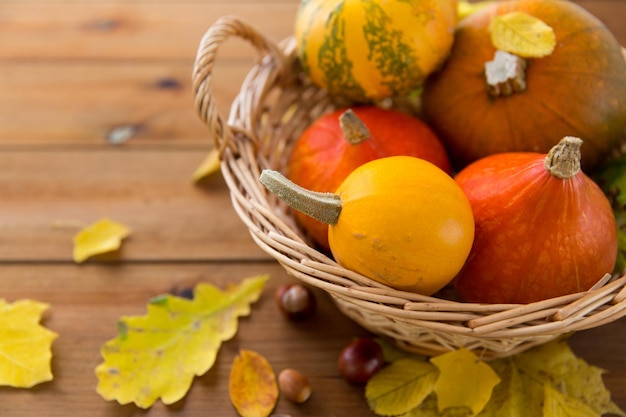 concepto de cosecha, temporada, publicidad y otoño - cierre de calabazas en una cesta de mimbre con hojas sobre una mesa de madera en casa